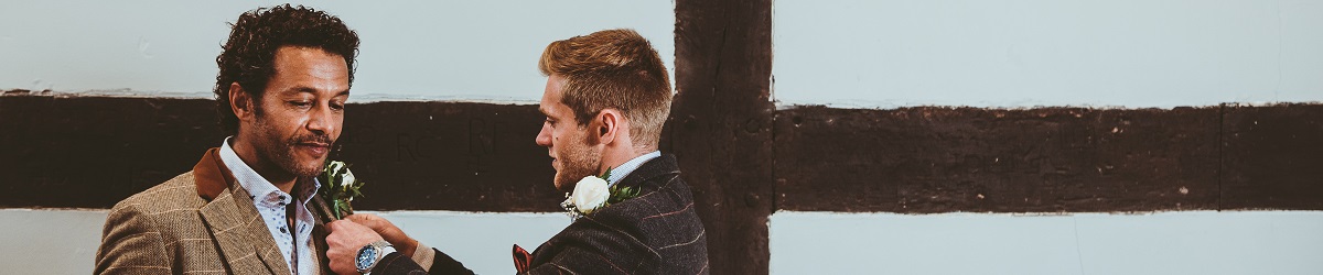 A best man fixes the buttonhole of a groom at a Tudoe Hall wedding reception with timber frames as a backdrop